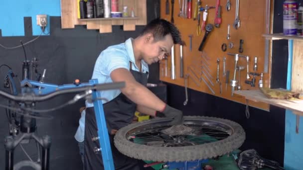 Механик велосипеда в фартуке в перчатках устанавливает колесо — стоковое видео