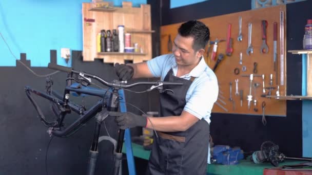 Ремонтнику в фартуке звонят по мобильному телефону во время ремонта велосипеда — стоковое видео