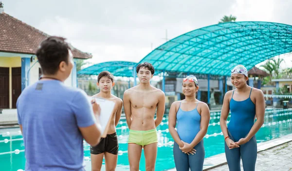 Quatre nageurs adolescents en maillots de bain debout avec entraîneur — Photo