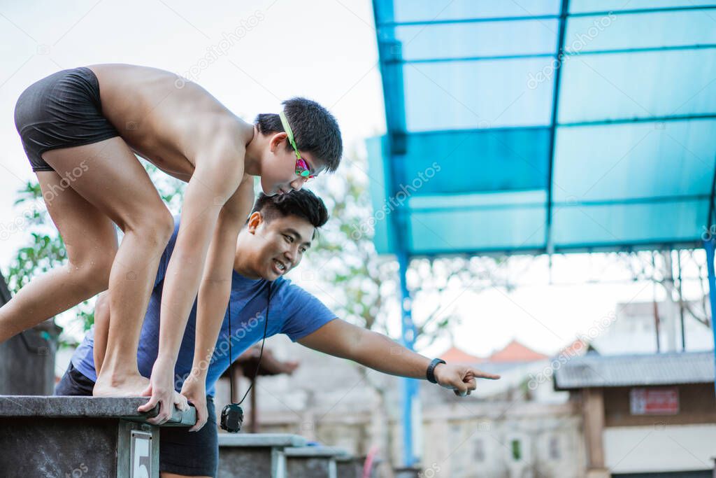 teenage swimmer standing on block board and getting ready to jump and swim with a coach