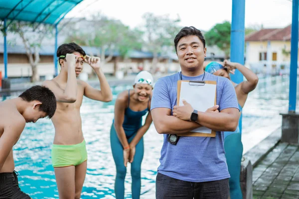 Улыбающийся азиатский тренер по плаванию с блокнотом и секундомером — стоковое фото