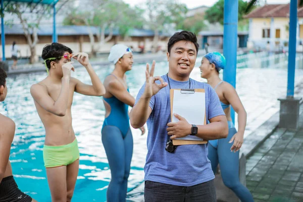 水泳のトレーナーは、クリップボードを保持しながら、 ［OK］を指ジェスチャーで笑顔 — ストック写真