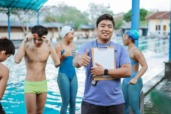 Ένας εκπαιδευτής κολύμβησης χαμογελά με τους αντίχειρες ψηλά, ενώ κρατώντας ένα πρόχειρο — Φωτογραφία Αρχείου