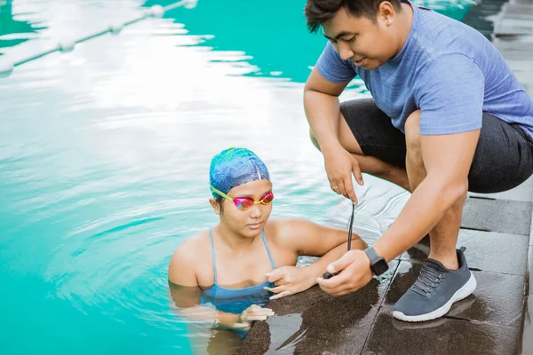 Ένας γυμναστής δείχνει το χρόνο με ένα χρονόμετρο σε μια νεαρή γυναίκα κολυμβήτρια — Φωτογραφία Αρχείου