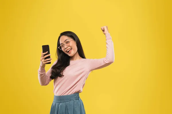 Woman in glasses smiling with one hand raised while using a smartphone — Stock Photo, Image