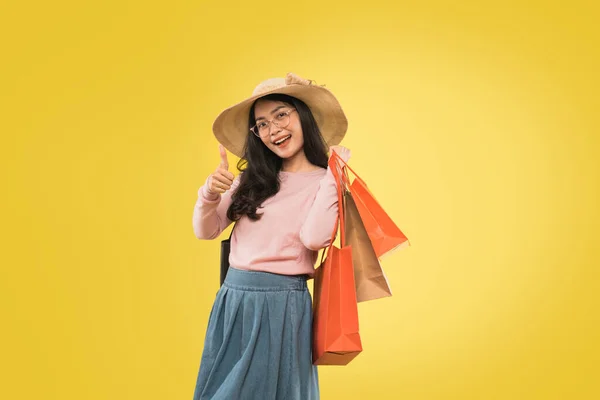 Jonge Aziatische vrouw in hoed en bril dragen shopping papieren zak met duimen omhoog — Stockfoto