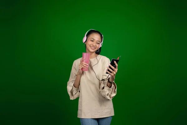 Jong meisje het dragen van een koptelefoon tijdens het drinken tijdens het luisteren naar muziek — Stockfoto