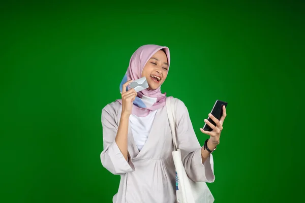 Женщина в хиджабе смеется во время использования мобильного телефона, держа банковскую карту — стоковое фото