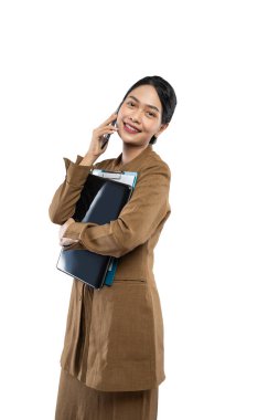 Üniformalı kadın öğretmen dizüstü bilgisayar taşırken telefonla arama yapıyor.