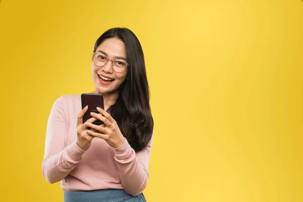 Mulher bonita em óculos sorrindo para a câmera ao usar um telefone celular — Fotografia de Stock