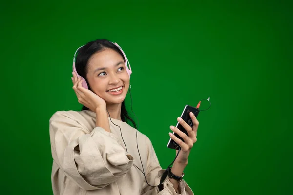 Flicka bär hörlurar och hålla en mobiltelefon medan du lyssnar på musik — Stockfoto