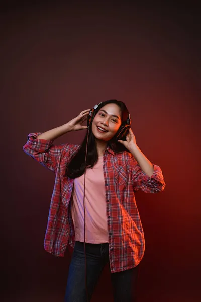 Весела дівчина насолоджується музикою за допомогою навушників з двома руками, тримаючи навушники — стокове фото