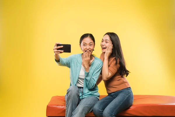 Upphetsad två asiatiska flicka med hjälp av en smartphone för att göra videosamtal tillsammans — Stockfoto