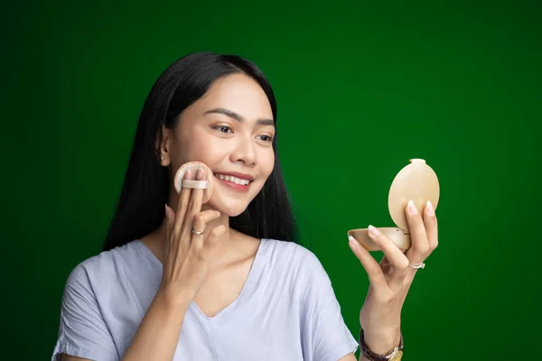 Beautiful woman smiling while using powder puff and holding small mirror while applying make up — Stock Photo, Image