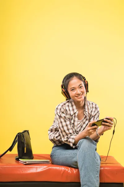 Menina asiática com fones de ouvido usando smartphone enquanto sentado com livros e saco — Fotografia de Stock