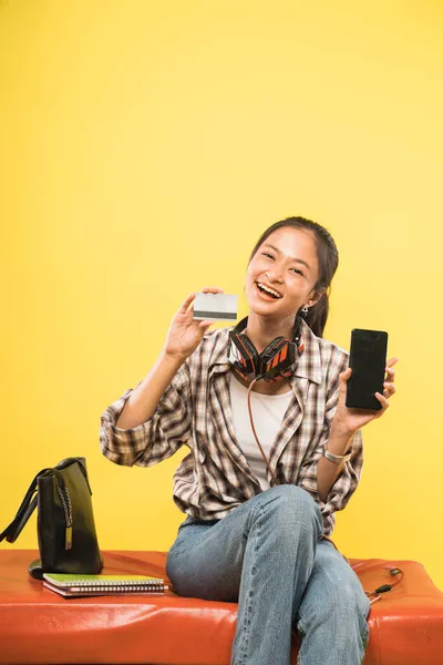 Student girl showing credit card and a smartphone while sitting on sofa — Stock Photo, Image