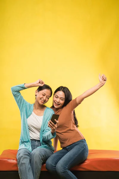 Aufgeregt zwei schöne asiatische Mädchen mit Händen nach oben, während suchen Smartphone — Stockfoto