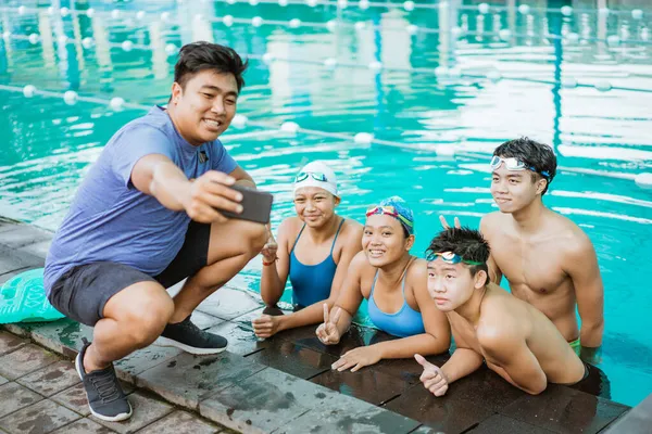 Um homem à beira da piscina tira uma selfie com quatro adolescentes vestindo maiôs em uma piscina — Fotografia de Stock