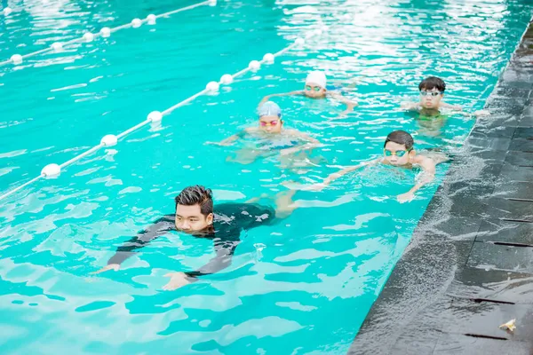 Инструктор дает пример того, как плавать в бассейне до четырех подростков — стоковое фото