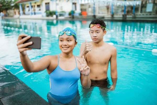 在游泳池里拿着智能手机自拍时，女人和年轻人都面带微笑 — 图库照片