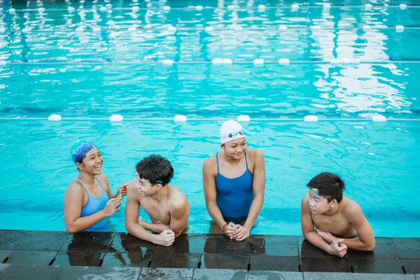 Czworo nastolatków w strojach kąpielowych na czacie podczas odkrytego basenu — Zdjęcie stockowe