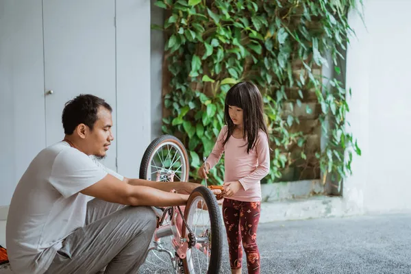 Niña sosteniendo una llave inglesa mientras pedalea con su padre — Foto de Stock