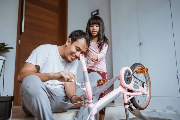 Азіатський батько робить з донькою невеличкий велосипед. — стокове фото