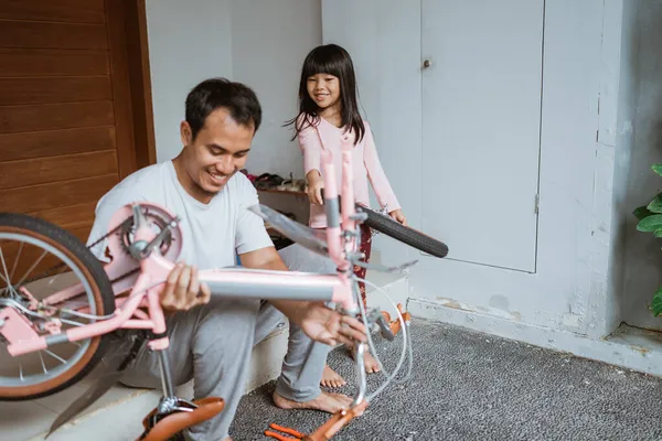 Joven padre sosteniendo el marco de la bicicleta y la hija llevando ruedas — Foto de Stock