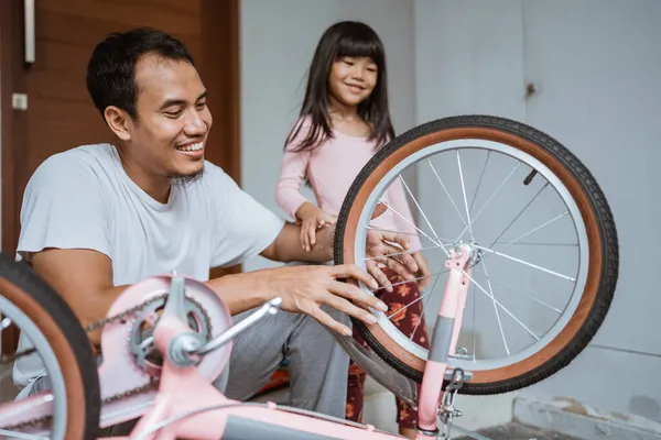 Батько ремонтує спиці велосипедного колеса з дочкою — стокове фото