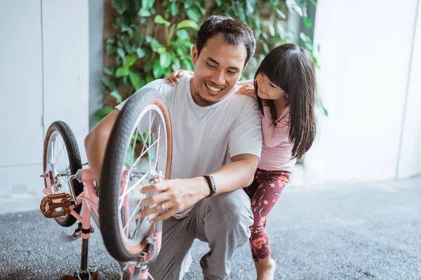 Joven asiático hombre con su hija reparación childs bicicleta rueda —  Fotos de Stock