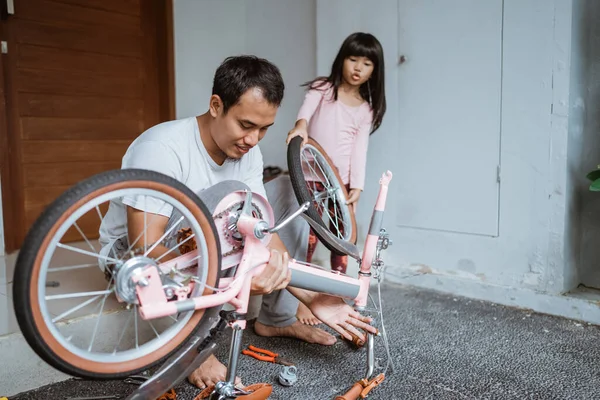 Asian father holding bicycle frame and daughter carrying wheels