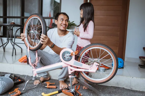 Asiatischer Vater sitzt mit Tochter beim Reparieren eines Fahrrads — Stockfoto