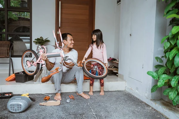 Father holding bicycle frame and daughter carrying wheels