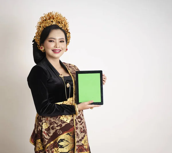 Χαμογελαστή γυναίκα από το Μπαλί φορώντας παραδοσιακά ρούχα που δείχνει ψηφιακή ταμπλέτα — Φωτογραφία Αρχείου