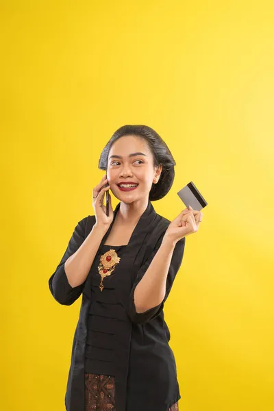 Kebaya 'lı mutlu Asyalı kadın kredi kartıyla telefon alışverişi yapıyor. — Stok fotoğraf