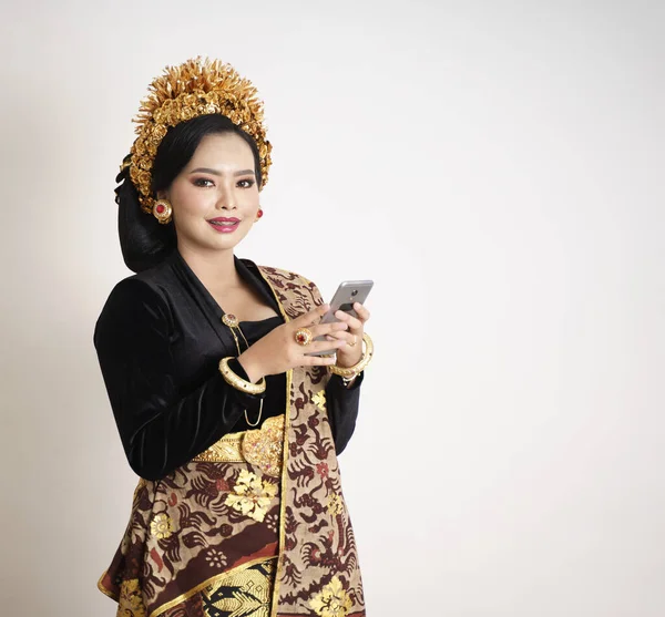 Χαμογελαστή γυναίκα από το Μπαλί φορώντας παραδοσιακά ρούχα χρησιμοποιώντας smartphone — Φωτογραφία Αρχείου