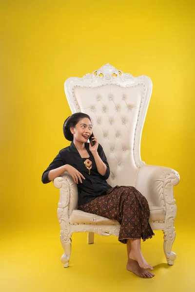 Wanita mengenakan Kebaya duduk di sofa saat membuat panggilan — Stok Foto