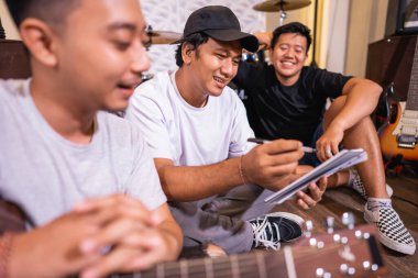 Genç Asyalı çocuk, arkadaşı gitar çalarken şarkı notaları yazıyor.