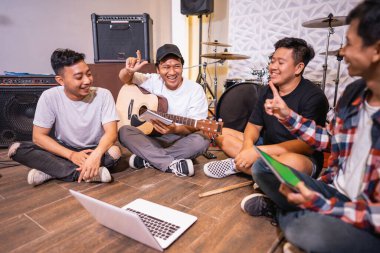 Dört kişi gitar çalıyor ve bir dizüstü bilgisayar kullanarak şarkıların video kliplerini izliyor.