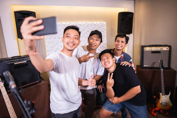 Four boys smiling while taking selfies with cellphone cameras while posing — Stock Photo, Image