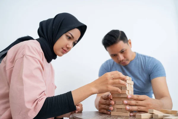 Kvinna i slöja och man arrangerar träklossar på bordet — Stockfoto