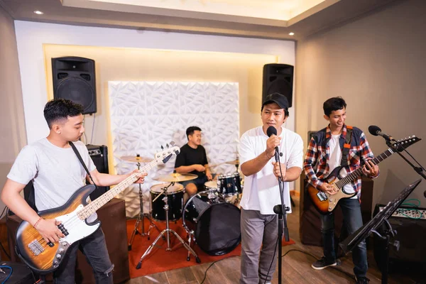 Four young men as a band sing songs and play musical instruments during sound check — Stock Photo, Image