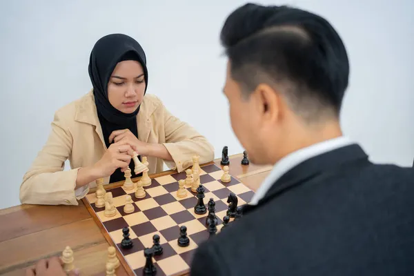 Donna in hijab che tiene pezzi di scacchi di fronte all'avversario che gioca a scacchi — Foto Stock