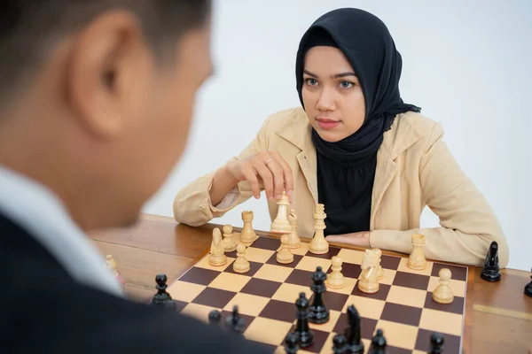 Kvinna i slöja som håller schackpjäser rör sig medan han spelar schack — Stockfoto