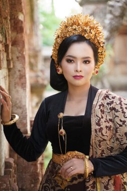 Endonezyalı kadın, Balili kebaya takmış, duvarın yanında.