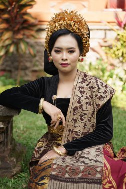 Balili kebaya giyen bir kadın bahçede oturuyor.