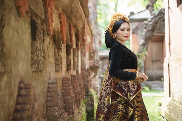 Chica vestida con kebaya balinés de pie cerca de la cerca de la pared de alivio — Foto de Stock