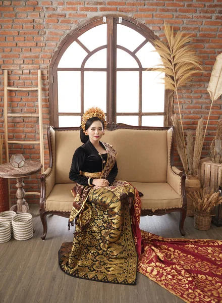 Женщина, сидящая на диване в ювелирных изделиях и балийской Кебайе — стоковое фото