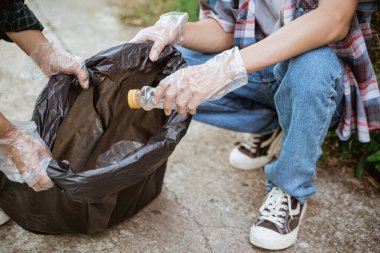 El plastik atıkları topluyor ve çöp torbasına koyuyor.