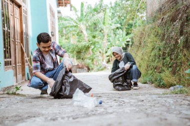 İki mutlu gönüllü genç çöpleri topluyor.